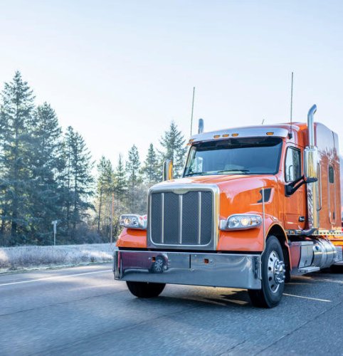Orange big rig American bonnet long haul semi truck with long cylindrical tank semi trailer transporting liquid and liquefied chemical cargo on the winter frosty road